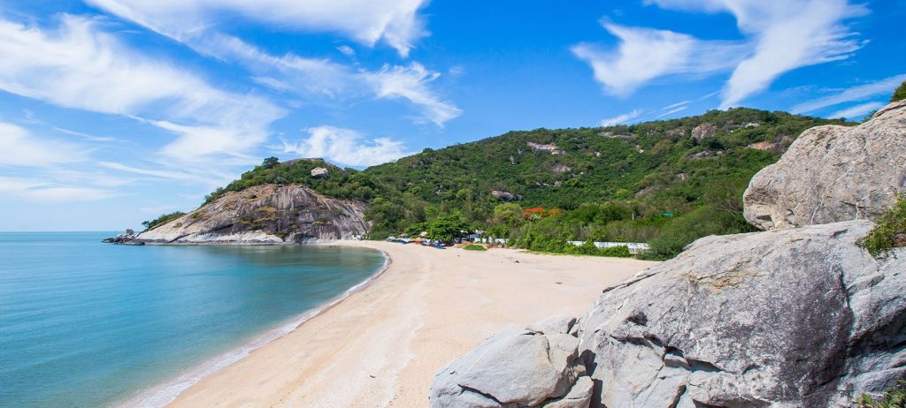 A sandy beach with rocks and a green headland